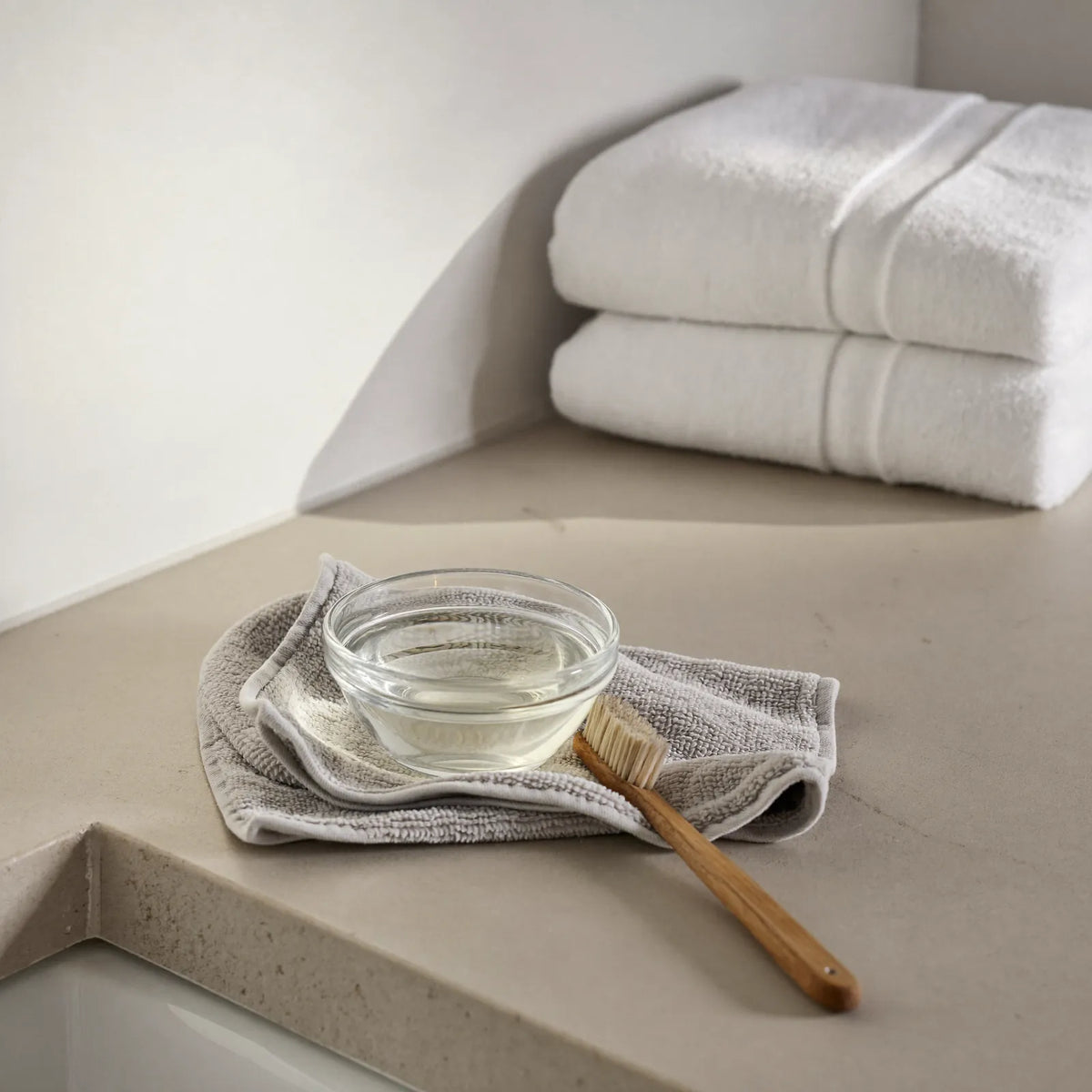 A calm, sunlit bathroom with white tiles, a folded towel and a chrome shower head resting in its holder