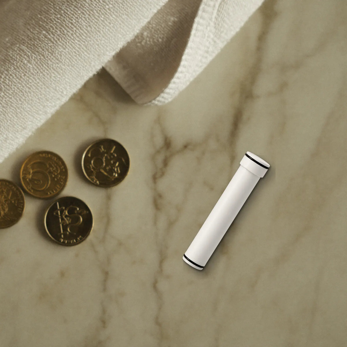 Gold and silver coins, some stacked, on a white marble shelf beside a folded white towel