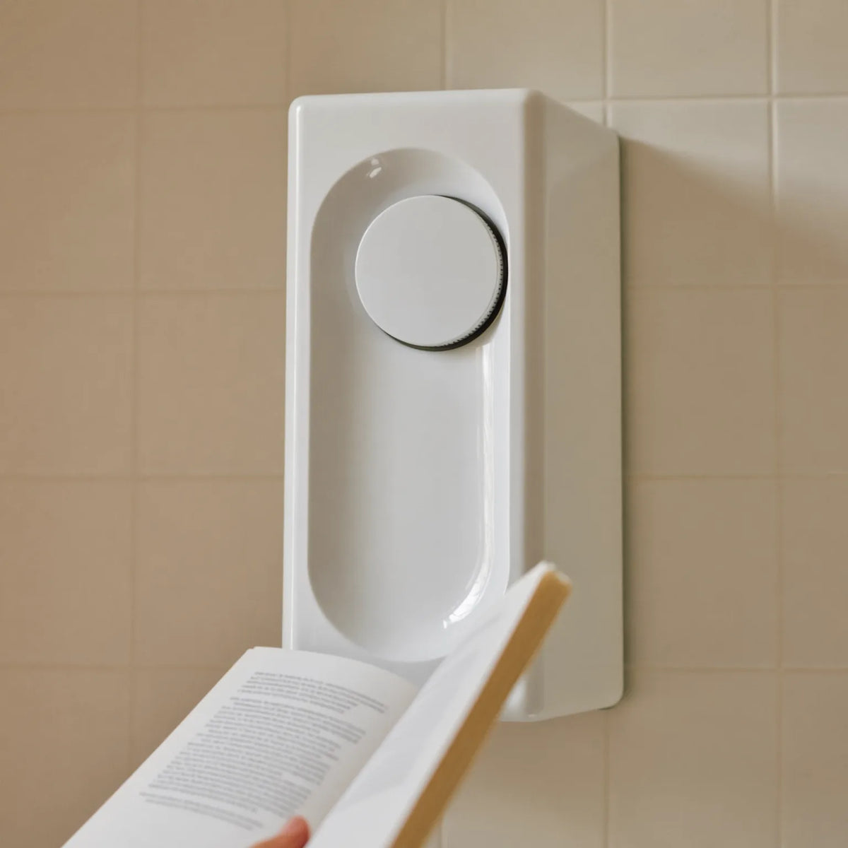 A plain white electric shower unit on cream tiles, with an open booklet held in the foreground