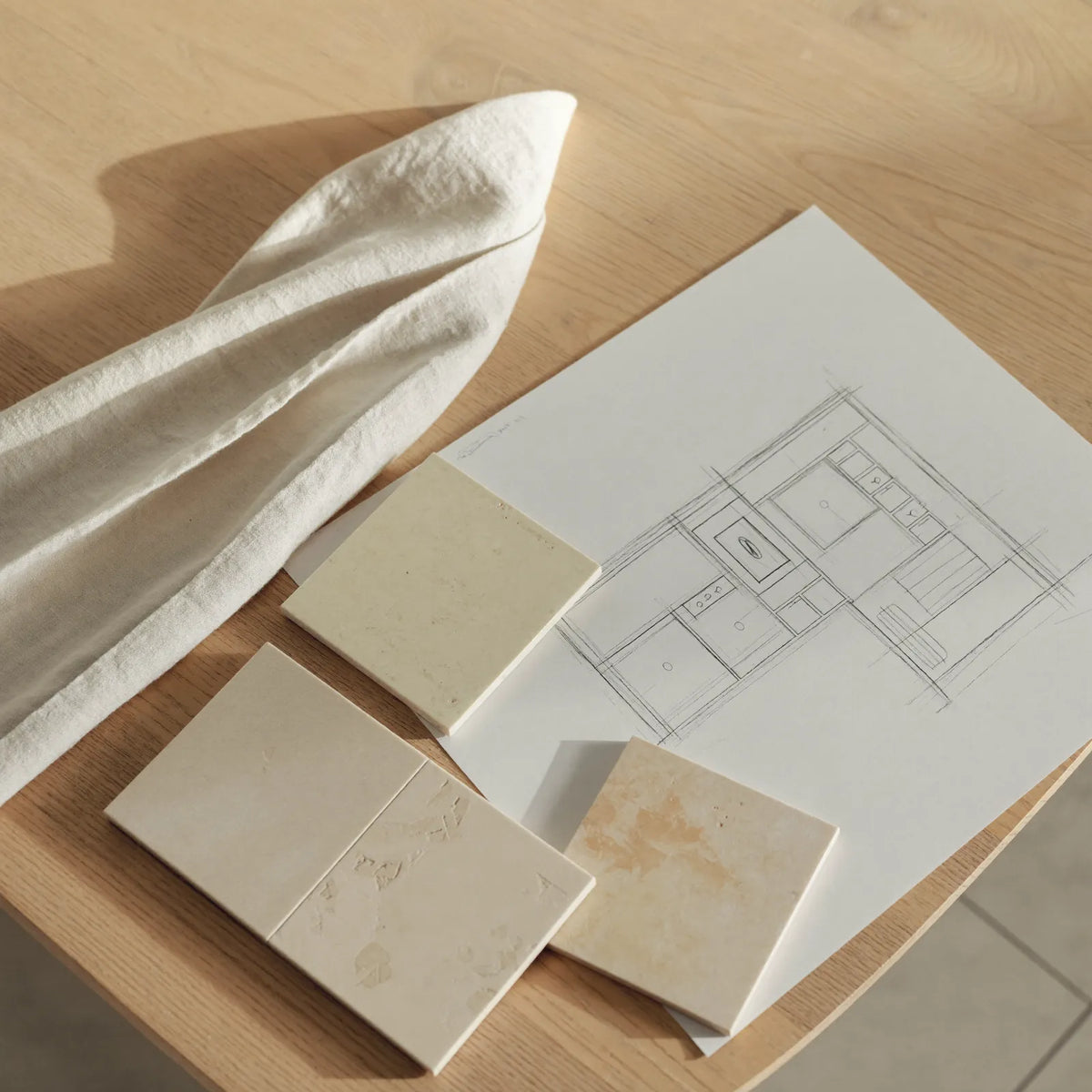 A calm, bright bathroom with a white bath, a folded towel on the edge and daylight falling across pale tiles